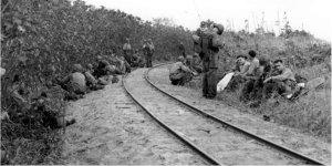 Photograph of troops resting besides a narrow-gauge
          railroad on Saipan